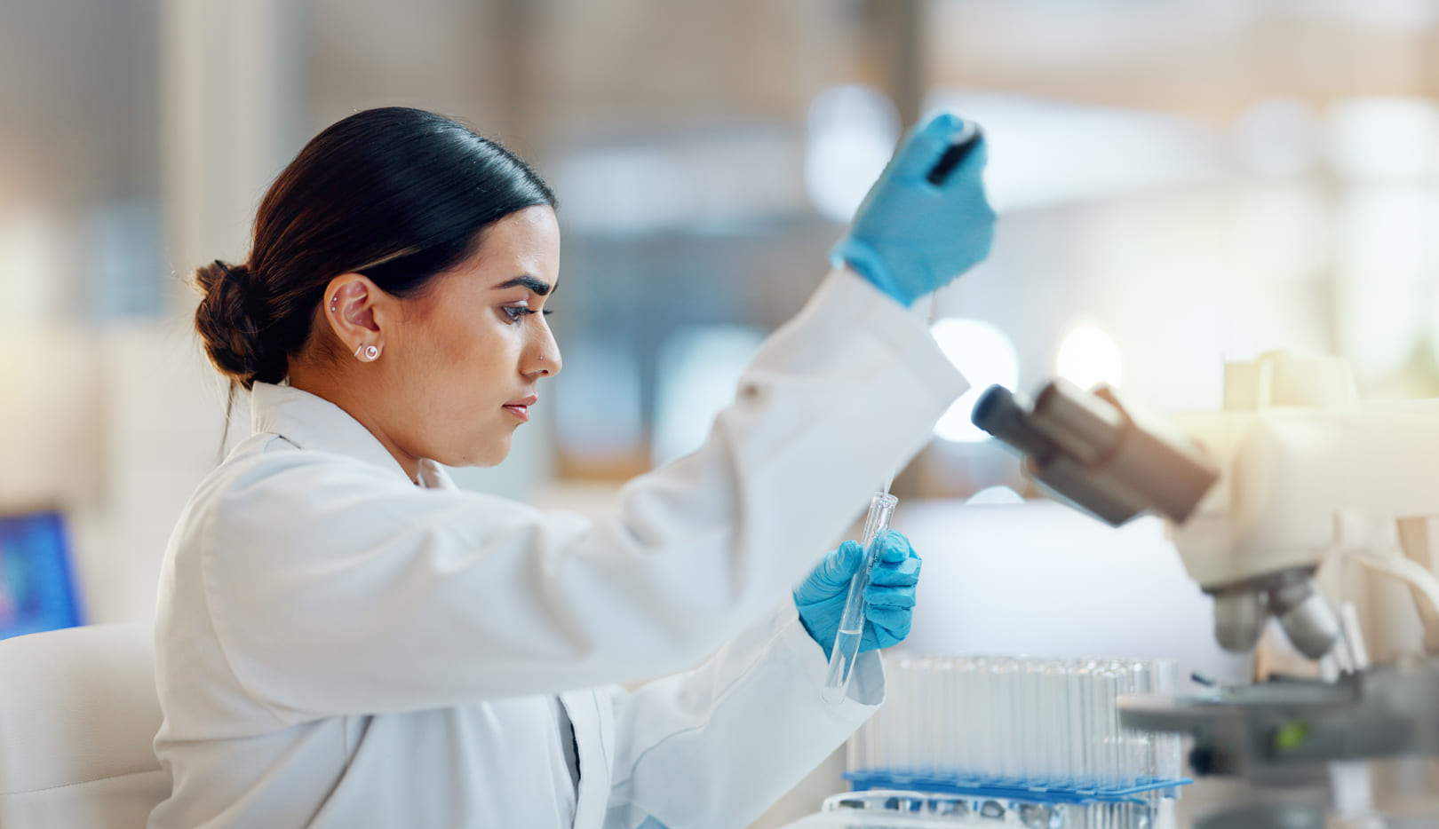 Researcher with pipette concentrates on test tube next to microscope