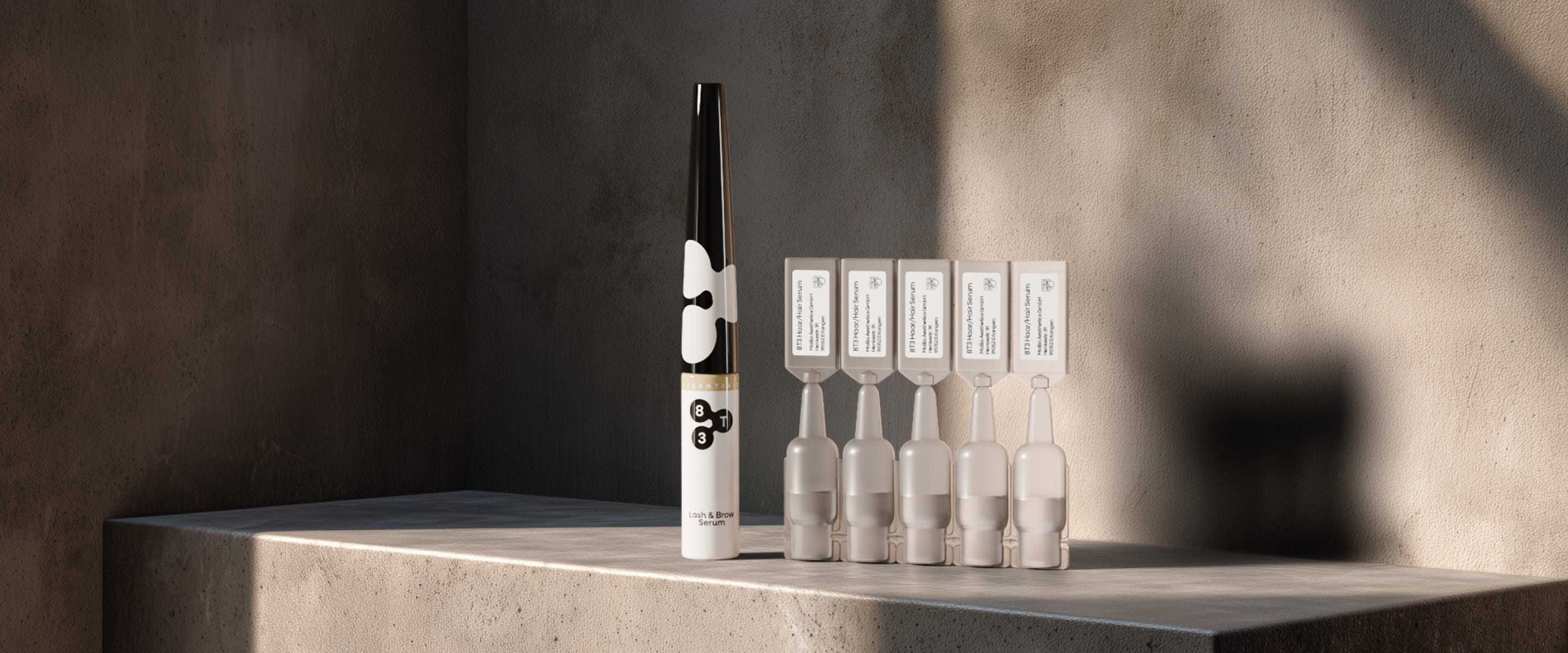Eyelash and eyebrow serum next to five hair serum ampoules on a concrete surface in side lighting