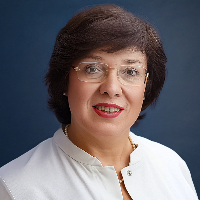 Portrait of a woman with short dark hair, glasses, and red lipstick wearing a white blouse against a blue background