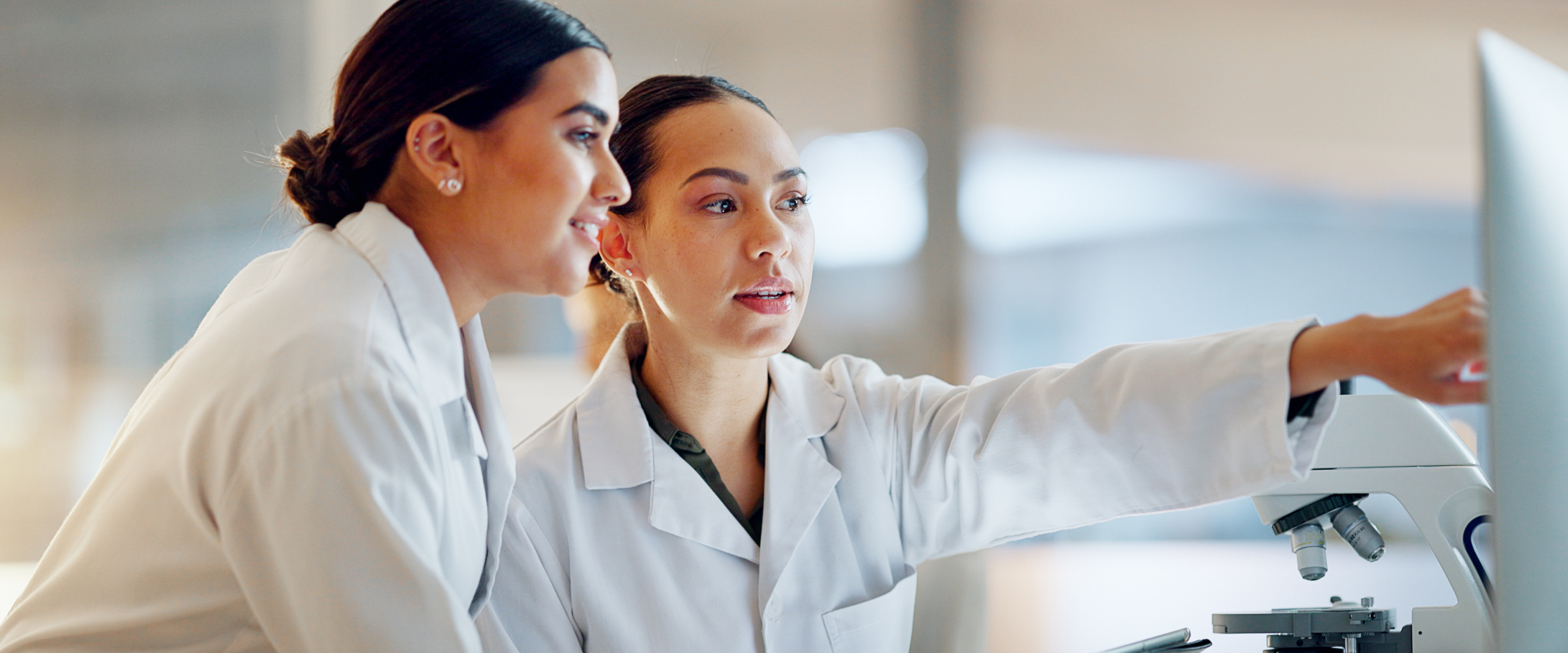 Two researchers in a laboratory pointing at a monitor next to a microscope