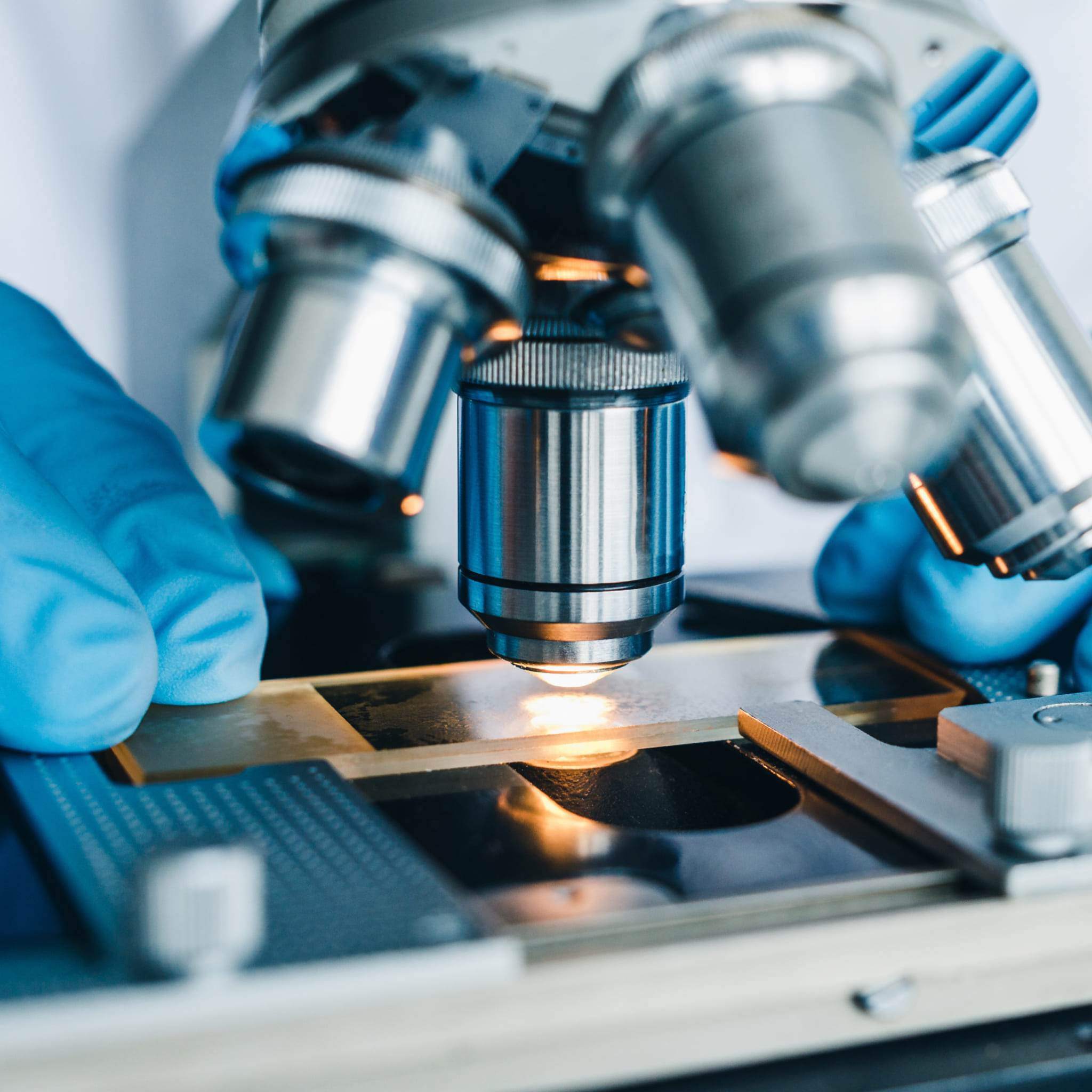 Illuminated lens of a microscope, gloved hand adjusting a microscope slide