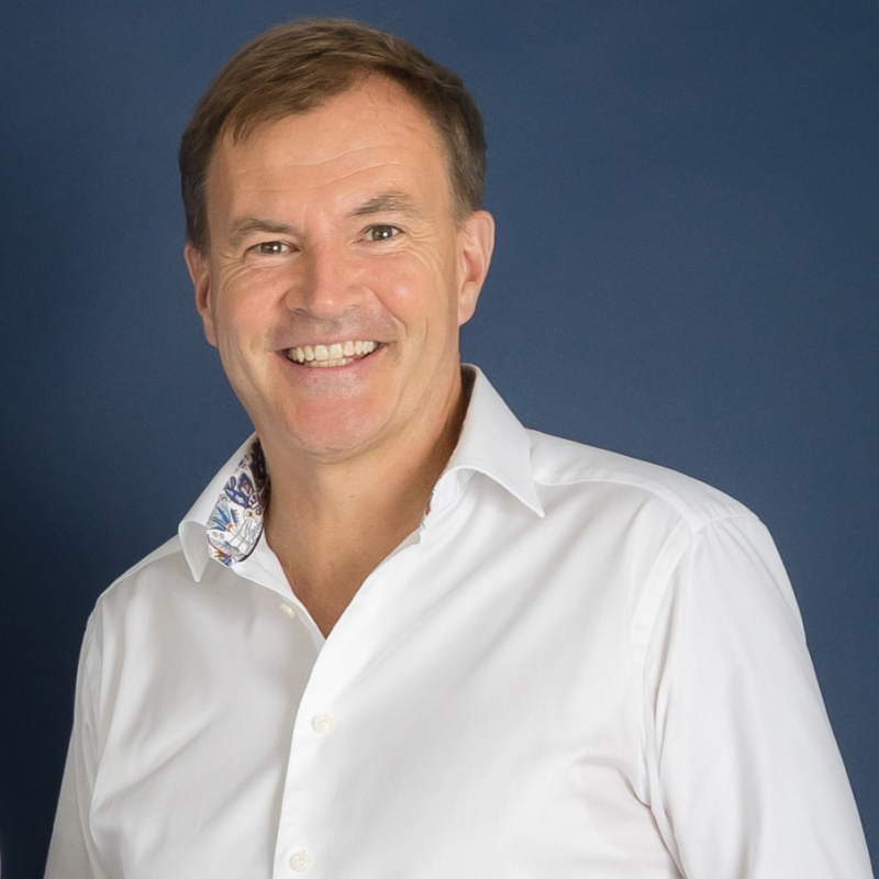 Portrait of a middle-aged man in a white shirt, smiling in front of a blue background.