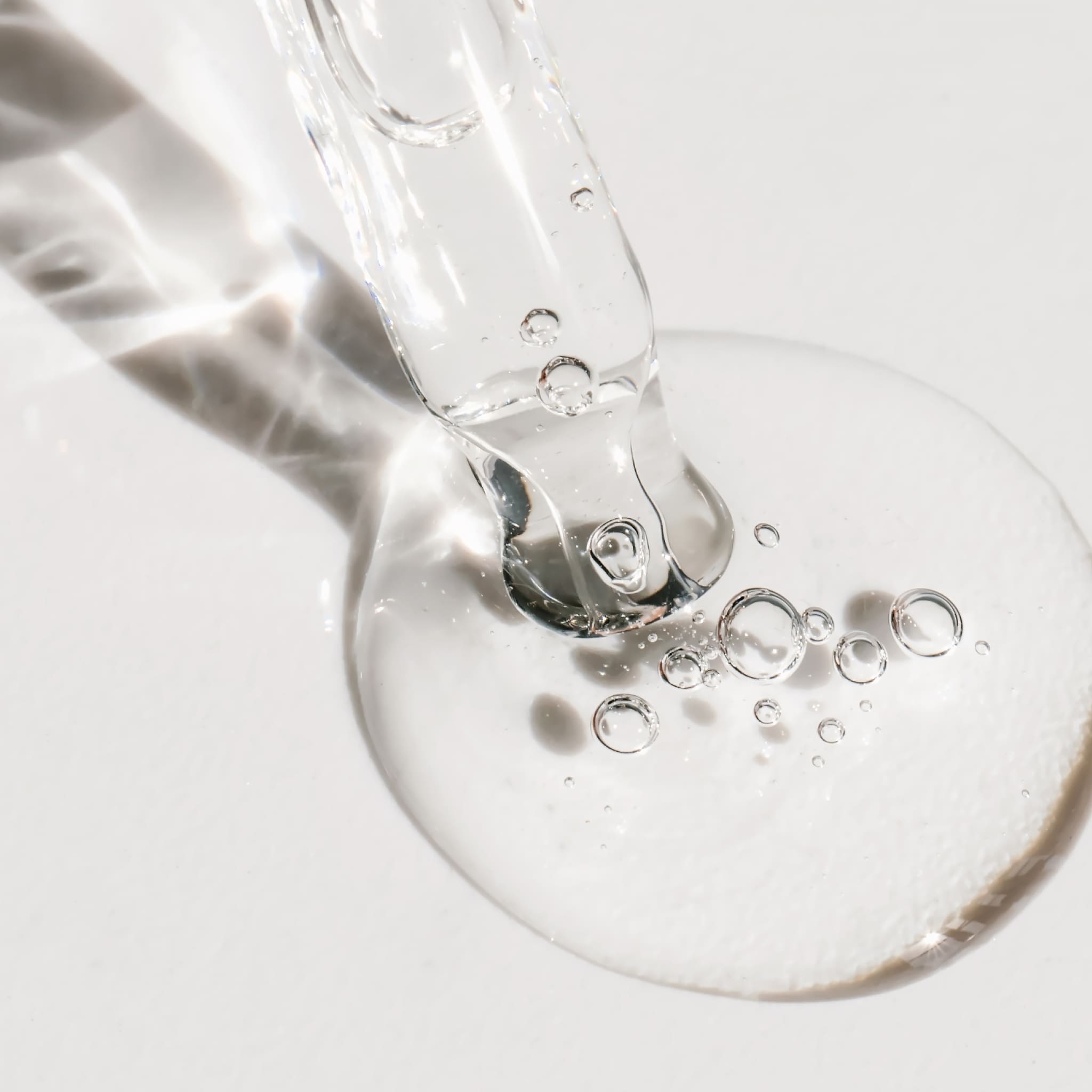 Macro shot of a clear gel with air bubbles dripping from a pipette onto a white surface