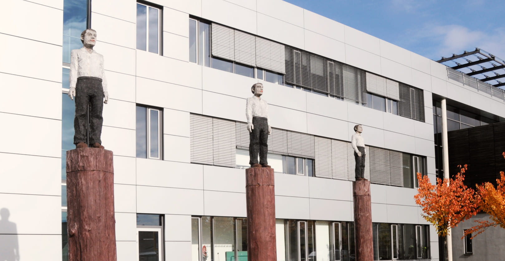 Modern building facade with three wooden sculptures on tall trunks in the foreground
