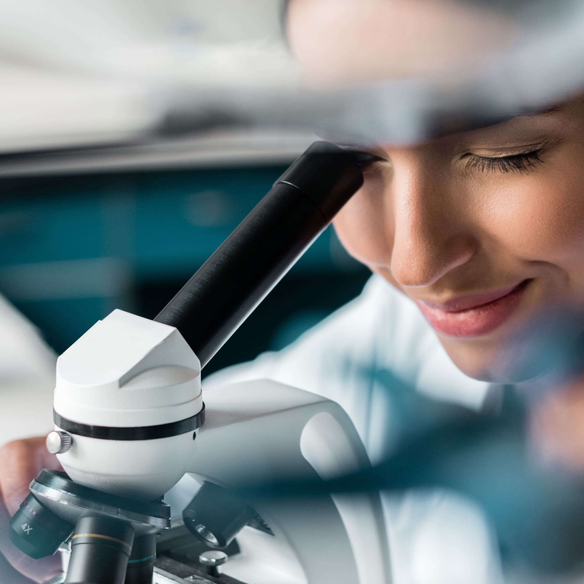 Scientist smiles and looks through a microscope in the laboratory.