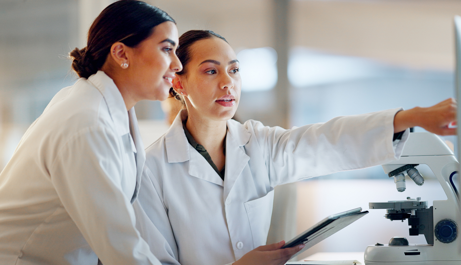 Two researchers in the laboratory view data on the monitor next to the microscope