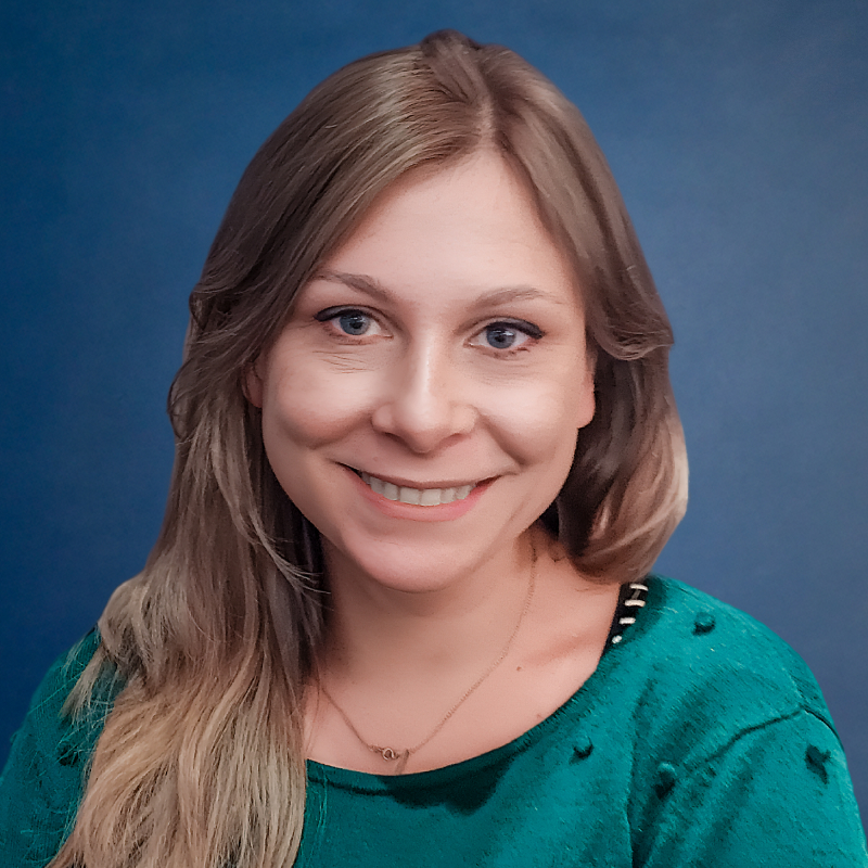 Portrait of a smiling woman with long light brown hair wearing a green top against a blue background.